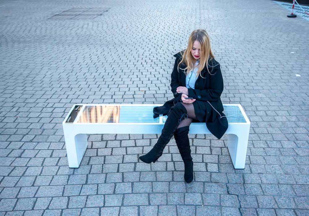 Vue en plein jour d'une femme assises sur un banc urbain connecté modèle stéora